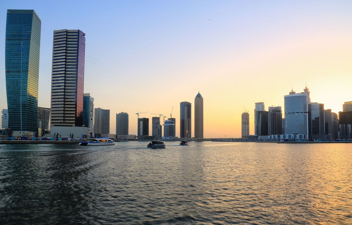 The Business Bay stretch of the Dubai Water Canal at golden hour, office and residential towers on both banks and a boat on the water