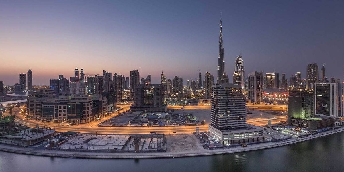 Business Bay at dusk from a height: the curve of the canal in front and the lit towers behind it