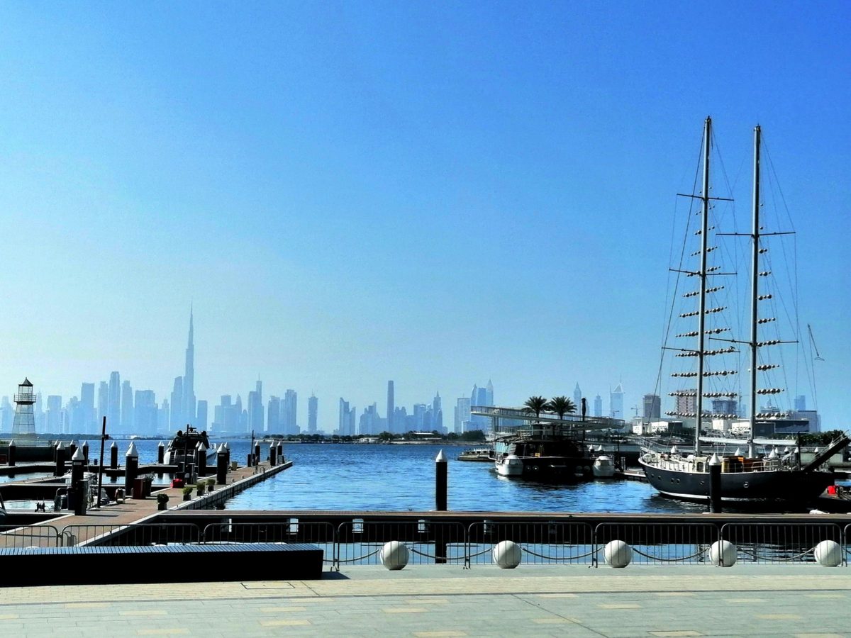 The Creek Marina promenade at Dubai Creek Harbour with pontoons and a two-masted yacht, the Downtown Dubai skyline across the water