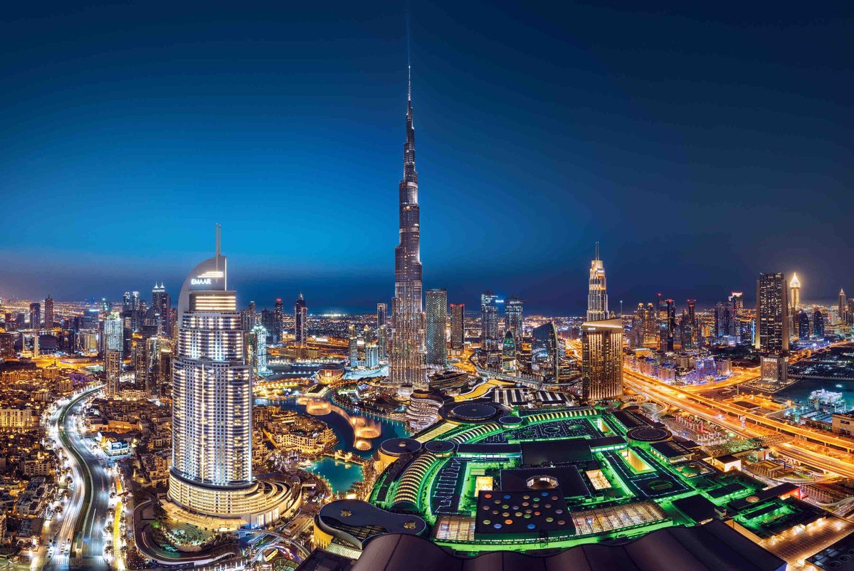 Downtown Dubai at night from a height: Burj Khalifa in the centre, the lit Dubai Mall roofs in front and the district's towers around them