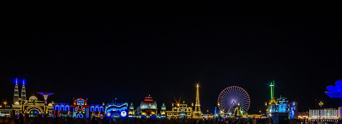 Global Village at night from outside: the lit pavilions and the Ferris wheel in one long row