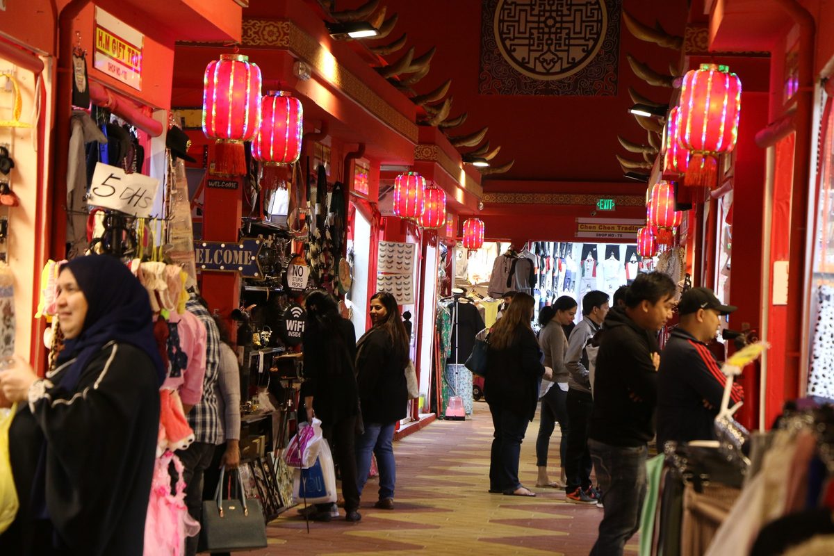 A covered market lane inside Global Village hung with red lanterns, shoppers between the stalls