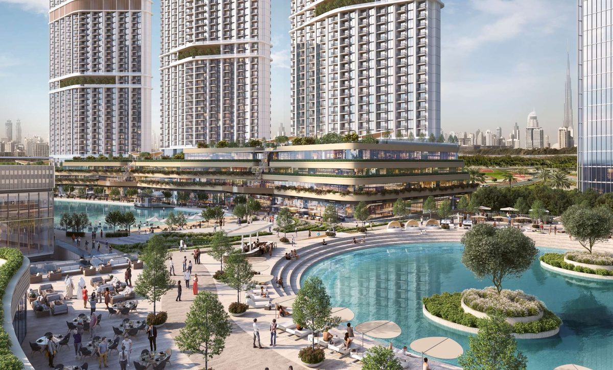 Sobha Hartland II from above its plaza: the lagoon and the terraced retail spine in front, the towers behind, Burj Khalifa on the horizon
