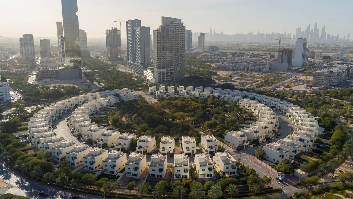 Jumeirah Village Circle from the air: Nakheel's ring of villas around a park, apartment towers by other developers behind and the Marina skyline in the haze