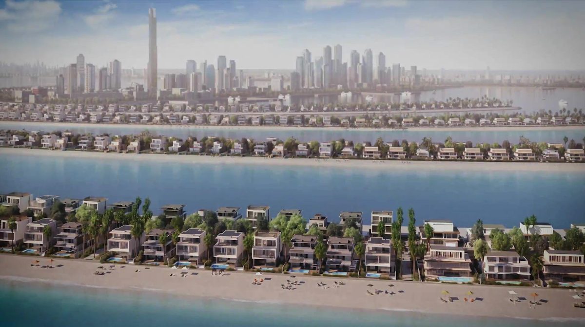 Low aerial along one frond of Palm Jebel Ali, villa rows on both sides, the Dubai skyline in the haze on the horizon — a frame of Nakheel's own film
