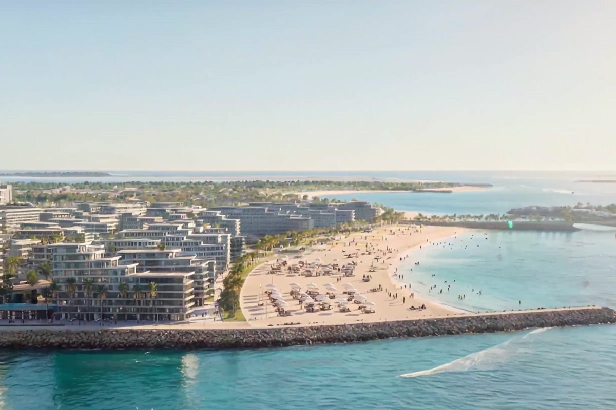 Aerial view of the district's beach: parasols and loungers along the sand, the breakwater and the low residential blocks behind
